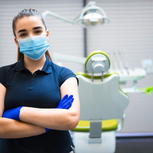 Young female dentist doctor in mask stands in the office with his arms crossed